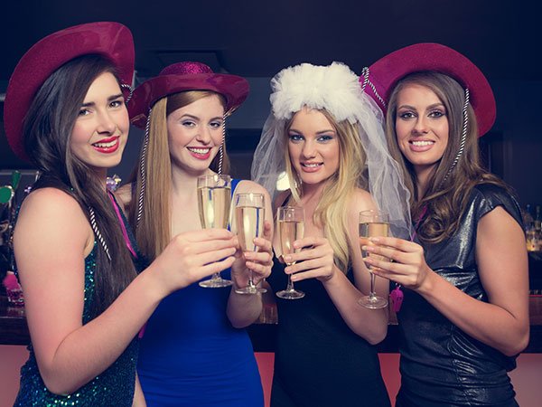 Young women on a hens party with hats on while bride to be is wears a white veil