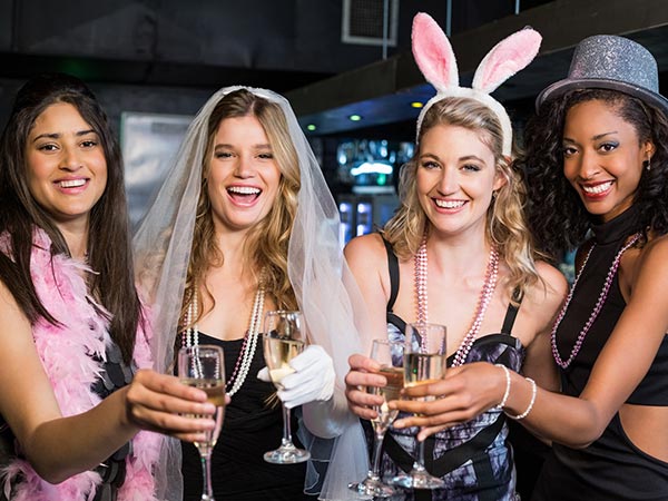 4 women with hens party accessories on including bunny ears, party hat, veil, feather boa and necklaces