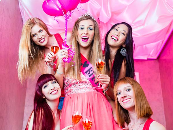 Bride to be with sash on holding balloons surrounding by her close friends all dressed in pink